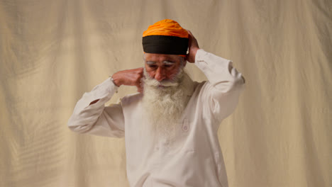 Studio-Shot-Of-Senior-Sikh-Man-With-Beard-Tying-Fabric-For-Turban-Against-Plain-Background-As-Sequence-Part-2-Of-3